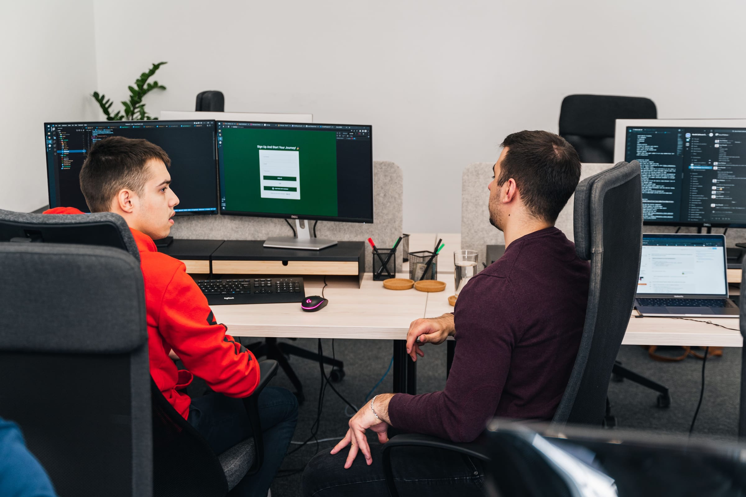 Two Nortik engineers talking at their desks with code on the monitors behind them